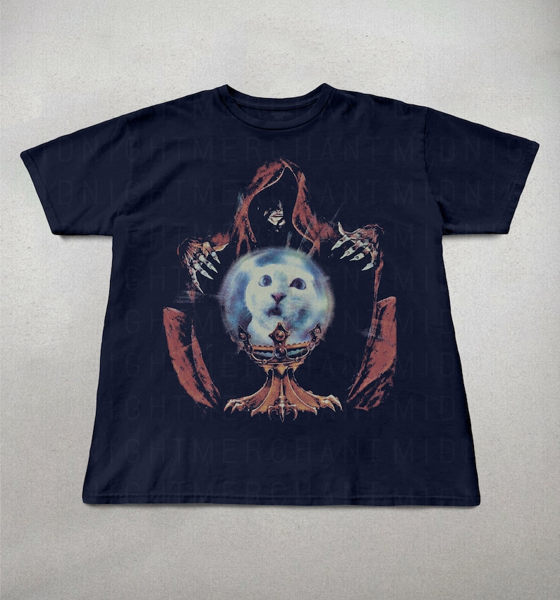 May include: Navy blue t-shirt featuring a graphic of a hooded figure with clawed hands, holding a glowing orb with a cat's face. The orb rests on a decorative chalice. The design is in shades of red, orange, and blue.