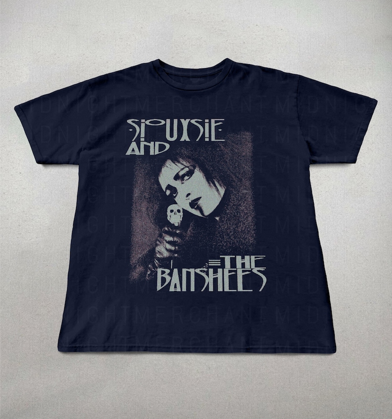 May include: Navy blue t-shirt featuring a graphic of Siouxsie Sioux and the band name, Siouxsie and the Banshees, in white text. The image shows a portrait of Siouxsie holding a skull. The shirt is a classic crew neck style.