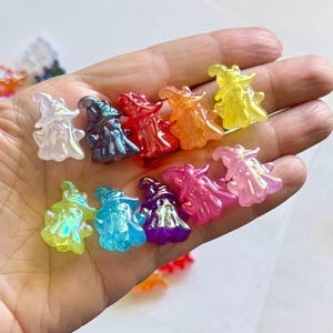 May include: A collection of small, translucent, ghost-shaped charms, each wearing a pointed hat. The charms are rendered in a variety of vibrant colors including yellow, orange, red, dark blue, light blue, purple, pink, and iridescent white.