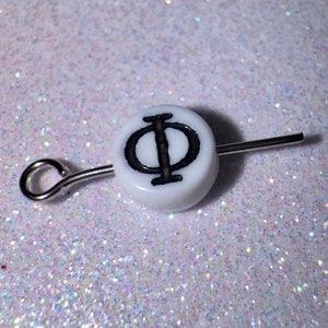 May include: White ceramic bead with a black Greek letter Phi symbol on it. The bead is attached to a silver wire with a loop at one end.