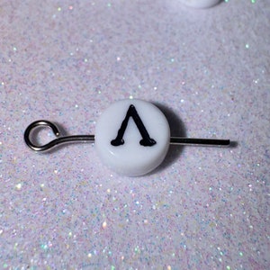 May include: White round bead with a black capital letter A on a silver wire.