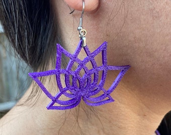 May include: Purple lotus flower earrings with silver hooks. The earrings are made of a textured material and have a delicate, intricate design.