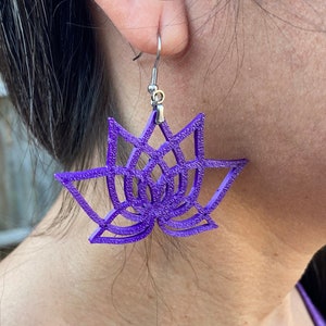 May include: Purple lotus flower earrings with silver hooks. The earrings are made of a textured material and have a delicate, intricate design.