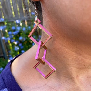 May include: Pink and gold geometric earrings with a square shape. The earrings are made of multiple squares that are linked together.