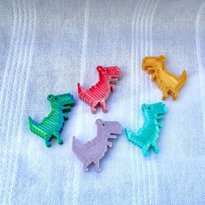 K&ouml;nnte beinhalten: F&uuml;nf kleine, 3D-gedruckte Dinosaurier-Figuren in verschiedenen Farben: Rot, Gr&uuml;n, Blau, Lila und Gelb. Die Dinosaurier sind alle in die gleiche Richtung ausgerichtet und in einem Halbkreis angeordnet.