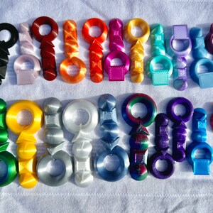 K&ouml;nnte beinhalten: Eine Sammlung von 20 bunten, 3D-gedruckten Schl&uuml;sselanh&auml;ngern. Jeder Schl&uuml;sselanh&auml;nger hat ein einzigartiges Design mit einem Ring oben zum Anbringen an Schl&uuml;sseln oder Taschen. Die Schl&uuml;sselanh&auml;nger sind aus Kunststoff und in verschiedenen Farben erh&auml;ltlich, darunter Rot, Blau, Gr&uuml;n, Gelb und Lila.