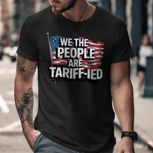 May include: Black t-shirt with a graphic of an American flag and the text "We the People are Tariff-ied".