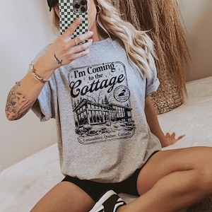 Könnte beinhalten: Ein meliertes graues Sweatshirt mit dem Text "I'm Coming to the Cottage" über einer Schwarz-Weiß-Illustration eines Ferienhauses. Das Sweatshirt hat auch den Text "Lanaudière, Québec, Canada".