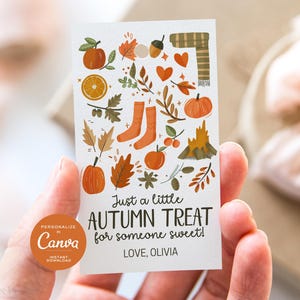 Op de afbeelding: Een rechthoekig cadeaulabel met herfstthema-illustraties, waaronder pompoenen, bladeren en sokken. De tekst luidt "Just a little AUTUMN TREAT for someone sweet!" en "LOVE, OLIVIA". Het label wordt in een hand gehouden.