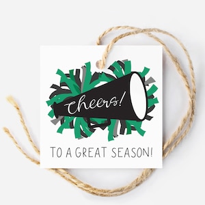 May include: A white gift tag with a black megaphone and green and gray pom poms. The text on the tag reads "cheers! to a great season!"