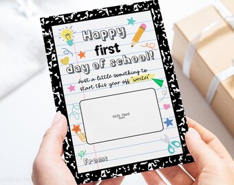 May include: A colorful gift card with a notebook paper design, featuring the text "Happy first day of school!" and decorative school-themed illustrations. Includes a space for a gift card and the text "From:"