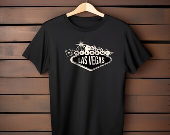 Può includere: Maglietta nera con una grafica argentata del cartello di Las Vegas con il testo "Benvenuti a Las Vegas" e icone a tema casinò.