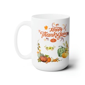 Puede incluir: Taza de café de cerámica blanca con un diseño de Acción de Gracias. La taza presenta una corona de hojas de otoño y calabazas con el texto "Happy Thanksgiving" en letras naranjas.