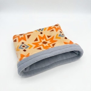 May include: A fleece neck warmer featuring a cream-colored base with a repeating geometric star pattern in orange, brown, and light blue. The interior and the folded top edge are lined with a solid light gray fleece fabric.