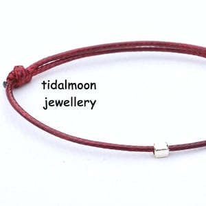 May include: Burgundy cord bracelet with a small silver bead. The bracelet is knotted at both ends. The text "tidalmoon jewellery" is visible in the image.