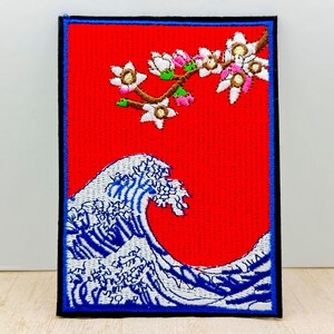 Peut inclure: Patch brodée thermocollante représentant une vague bleue et blanche avec une branche de fleurs roses et blanches sur fond rouge.