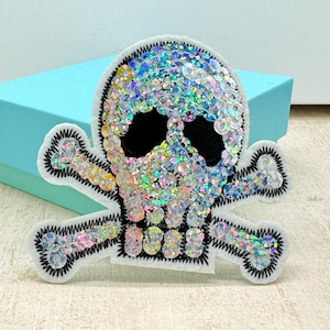May include: A white felt patch with a black and iridescent sequin skull and crossbones design.
