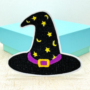 May include: Embroidered black witch hat patch with white edging, decorated with yellow stars and crescent moons. The hat has a purple band with a gold buckle. Ideal for Halloween or costume projects.