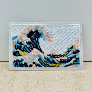 Peut inclure: Un patch brodé représentant un motif de vague bleu et blanc, rappelant la célèbre œuvre japonaise "La Grande Vague de Kanagawa".