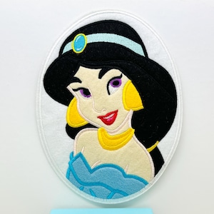 May include: A felt applique of Princess Jasmine from Disney's Aladdin. She is wearing a blue and white head scarf, a gold necklace, and a blue dress. Her hair is black and she has purple eyes.