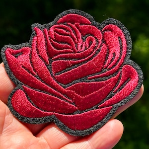 May include: A red embroidered rose patch with black stitching. The rose is a classic floral design and is perfect for adding a touch of elegance to any project.