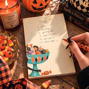 May include: A rectangular notepad with a cream-colored background featuring a printed illustration of a teal pedestal bowl filled with assorted candies. The text Today: includes a checklist with items: coffee, laundry, grocery run, clean kitchen, self care, and movie night.