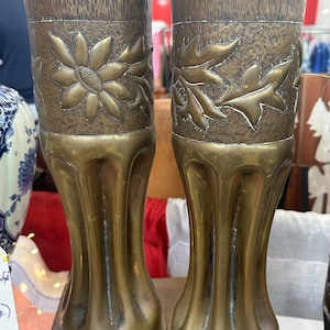 Puede incluir: Dos jarrones antiguos de latón con diseños florales en relieve. Los jarrones tienen una base acanalada y una boca ancha.