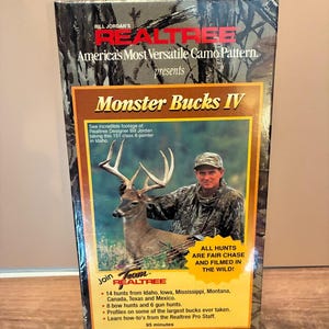 May include: A rectangular VHS tape box titled Monster Bucks IV featuring a Realtree camouflage pattern. The cover displays a photograph of a person in camouflage clothing with a deer, along with text detailing 14 hunts and 95 minutes of footage.