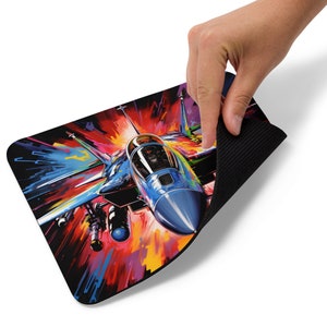 May include: A vibrant mousepad featuring a stylized illustration of a blue fighter jet in flight. The artwork showcases a dynamic composition with bold strokes of red, orange, yellow, and blue, creating a sense of speed and energy. The mousepad has a black, textured backing.