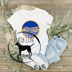 May include: White t-shirt with a blue and yellow circle design that says "Braves" in a white script font. The circle is surrounded by a leopard print pattern.