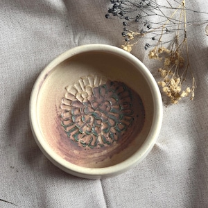 May include: A small, white ceramic bowl with a brown and green floral design. The bowl is ideal for serving small snacks or dips.