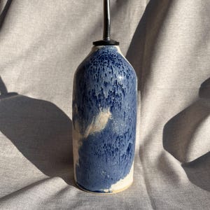 May include: A blue and white ceramic oil and vinegar bottle with a silver spout. The bottle has a mottled glaze with a white and blue marbled effect.