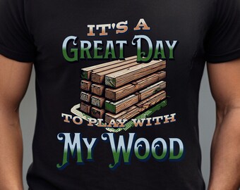 Op de afbeelding: Zwart T-shirt met een afbeelding van gestapelde houten blokken. De tekst "It's a Great Day to Play with My Wood" staat op het shirt gedrukt.