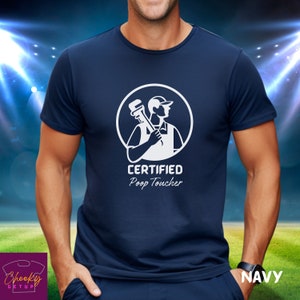 May include: A navy blue t-shirt with a white graphic of a plumber holding a wrench. The graphic is inside a circle with the text "CERTIFIED Poop Toucher".