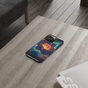 Puede incluir: Una funda para teléfono con un diseño de nebulosa colorido. La funda tiene un borde negro y un recorte para la cámara. El diseño de nebulosa presenta un centro naranja brillante rodeado de nubes azules y moradas.