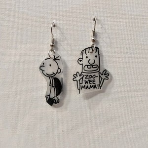 May include: A pair of silver earrings featuring transparent plastic charms with black line drawings of a cartoon character. One charm has the text "Zoo-Wee Mama!" printed on it.