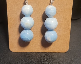 May include: A pair of dangle earrings with three light blue round beads on each earring. The beads have a white marbled pattern.