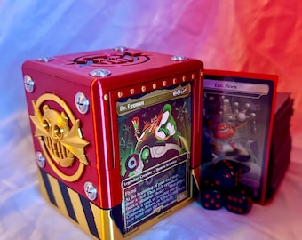 May include: A red and gold card storage box with a Dr. Eggman card visible. The box has a steampunk design with gold accents and black and yellow stripes. A stack of cards and dice are next to the box.