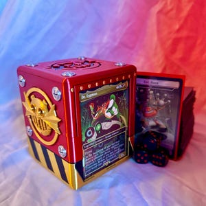 May include: A red and gold card storage box featuring a Dr. Eggman card. The box has a steampunk design with gold accents and black and yellow stripes. A stack of cards and dice are next to the box.