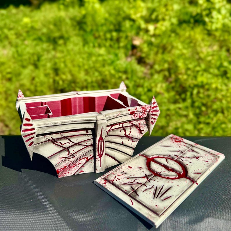 May include: A white and red decorative box with a matching lid. The box has a unique design with red accents and a splatter effect. The lid features a circular design. The box is open, revealing a red interior.