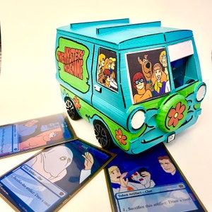 May include: A 3D-printed model of the Mystery Machine van from Scooby-Doo, in turquoise and green, with the show's logo on the side. The van has cartoon characters in the windows and is accompanied by collectible cards with the word "CLUE".