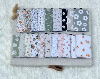 May include: A collection of rectangular cardholders with various floral, fruit, and patterned designs. The cardholders are arranged on a neutral-toned surface, showcasing a variety of colors and styles, including daisies, bows, and peaches.