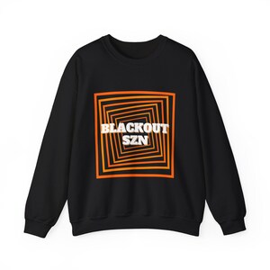 May include: Black sweatshirt with a graphic design of a square with concentric orange and yellow lines. The text "BLACKOUT SZN" is in white letters inside the square.