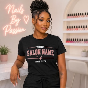 Op de afbeelding: Zwart T-shirt met roze tekst "YOUR SALON NAME", een afbeelding van een nagellakfles en de woorden "NAIL TECH". Een neonbord met "Nails By Passion" is zichtbaar op de achtergrond.