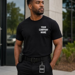 May include: Black crew neck t-shirt with the text "YOUR COMPANY NAME" in white. The person is wearing black pants, a black belt, and a security badge. A walkie-talkie is attached to the belt.