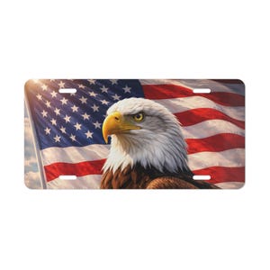 May include: Rectangular license plate featuring a majestic bald eagle with a yellow beak and piercing gaze. The background showcases a waving American flag with red and white stripes and a field of blue stars. The plate has pre-drilled holes.