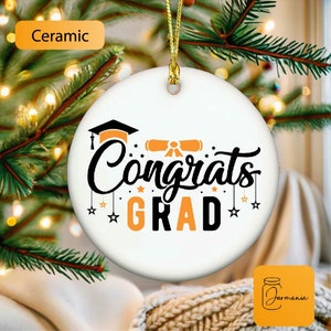 Peut inclure: Ornement en céramique blanche avec un motif de graduation noir et orange. L'ornement présente le texte "Congrats Grad" avec un bonnet de graduation et un diplôme.