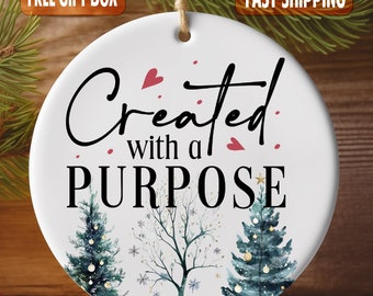 May include: White round Christmas bauble with a watercolour design of two trees and snowflakes. The bauble has the text "Created with a PURPOSE" in black script with red hearts.