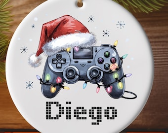May include: A white ceramic ornament with a red and white Santa hat and a black video game controller with colorful lights. The text "Diego" is printed in a pixelated font.