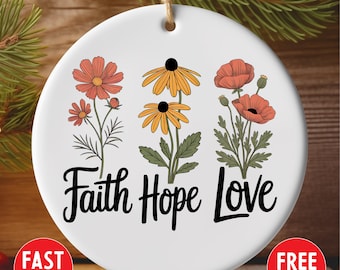 May include: Round white ceramic ornament with a floral design. It features orange and yellow flowers and the words "Faith Hope Love" in black script. The ornament has a string for hanging.